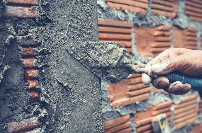 Trowel applying fresh parging over brick during water damage repair